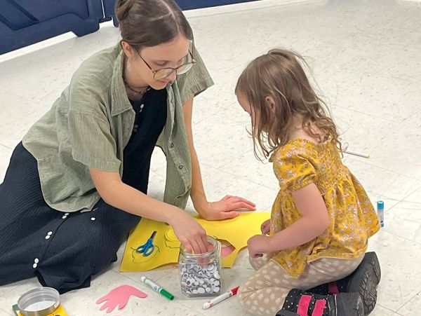 A woman and a young girl doing a craft project on the floor.