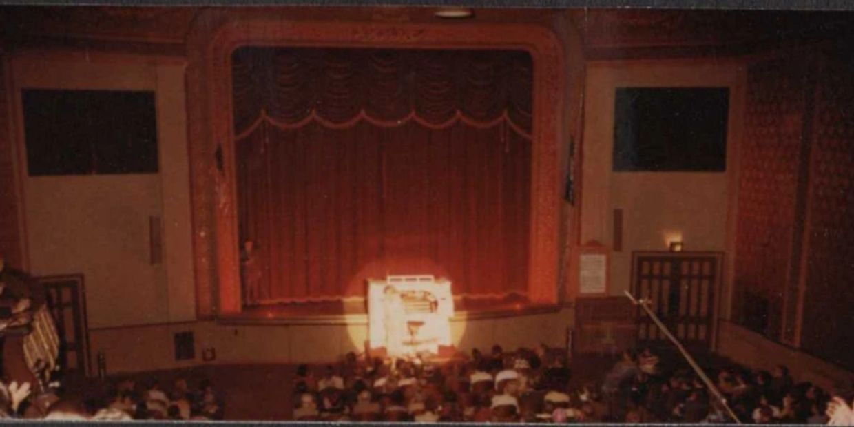 Audience watching a spotlighted stage with a piano.