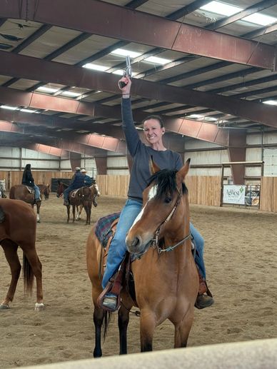 Woman on horse holding a revolver raised in an indoor arena.