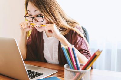 Female biting on a pencil in anticipation of an online auction while looking at a computer.