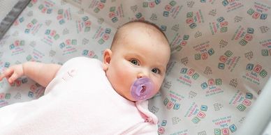 Baby with a pacifier lying in a crib with patterned sheets.