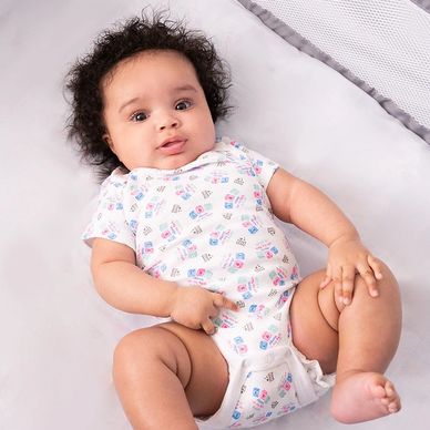 Adorable baby with curly hair lying on a white bed in a printed onesie.