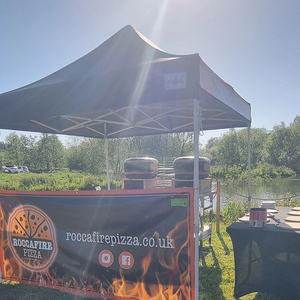 Outdoor pizza stall with a bright sunlit canopy and fiery banner.