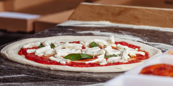 Unbaked pizza with tomato sauce, cheese, and basil on a floured surface.