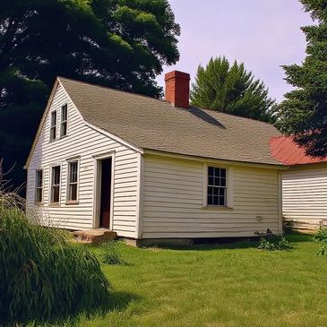 Small white house with chimney surrounded by greenery.