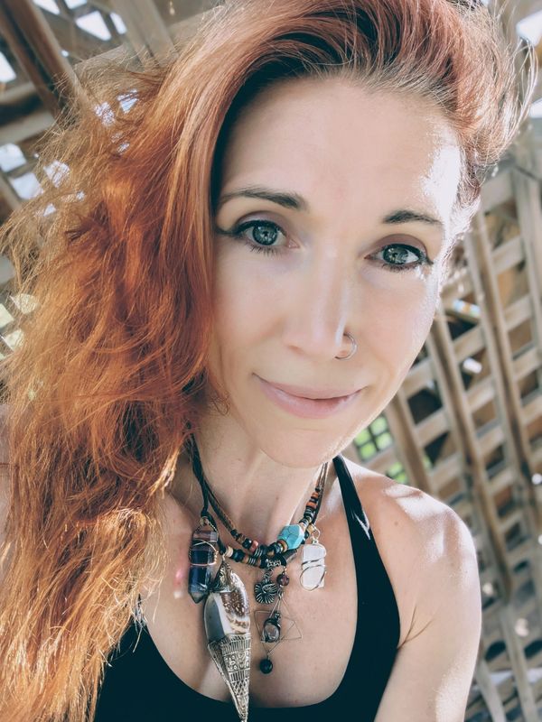 Andrea with red hair and blue eyes, smiling warmly, wearing a crystal and seashell necklace