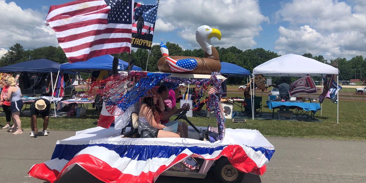 Patriotic parade float on a decorated golf cart with American flags, red, white, and blue streamers, and an inflatable bald eagle, participating in an outdoor festival under a sunny sky