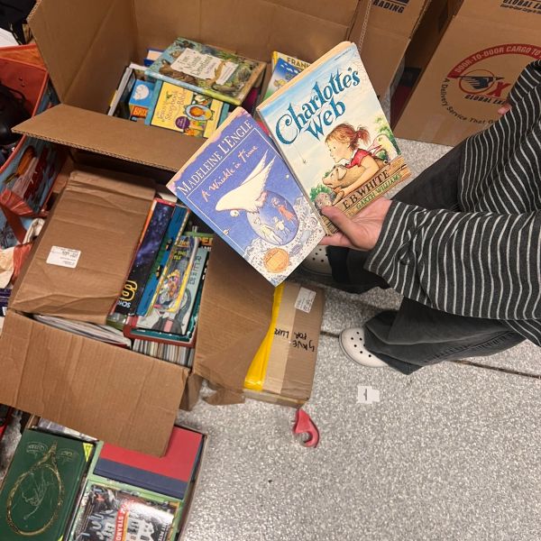 A person holding two classic children's books near open boxes filled with more books.