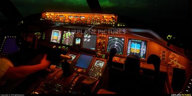 Cockpit of an airplane illuminated at night with pilots at controls.