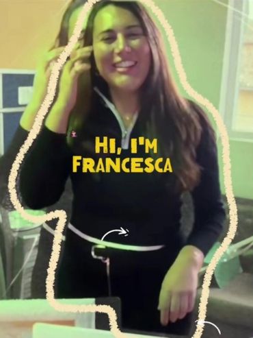 A woman named Francesca introduces herself with a smile indoors.