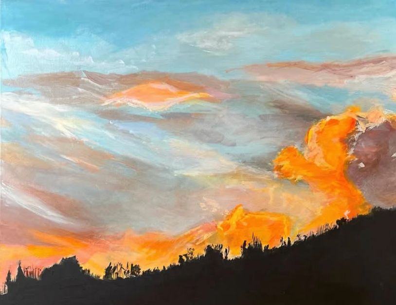 A vibrant sunset sky with orange clouds over a dark silhouette of trees.