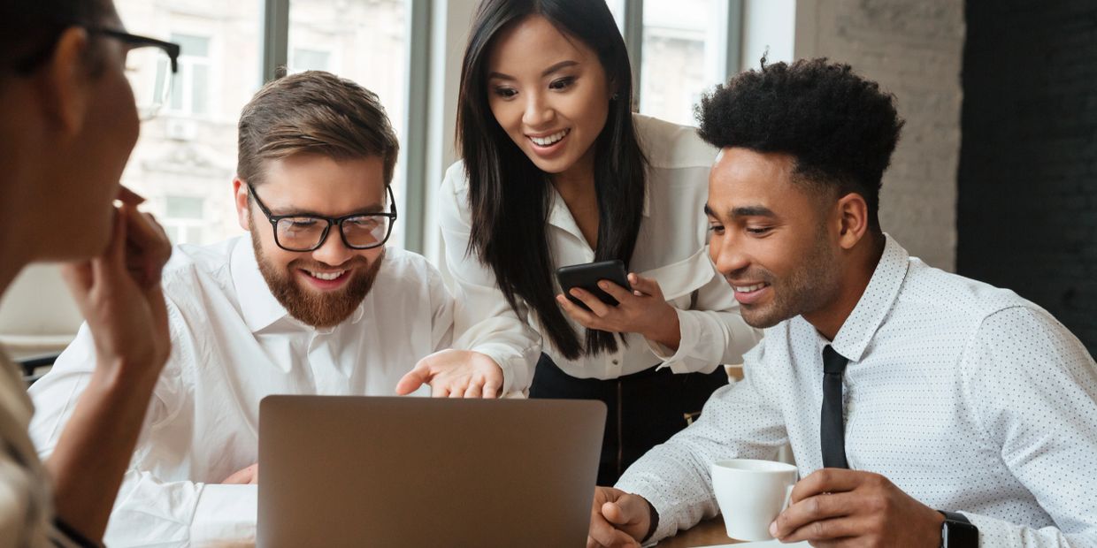 A diverse group of professionals happily collaborating over a laptop in an office.