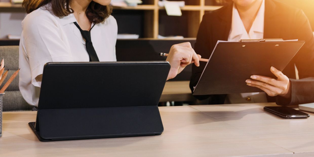 Two professionals discussing work with a tablet and clipboard in hand.