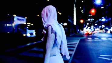 Person walking at night with a cloth over their head.
