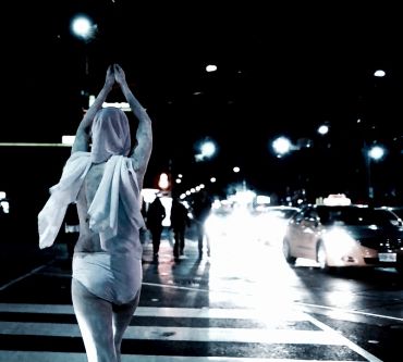 Person standing with hands raised on crosswalk at night.