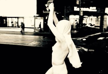 Person in white with arms raised in a dark urban setting.
