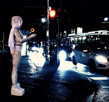 Figure in white with a sunflower at night in traffic.