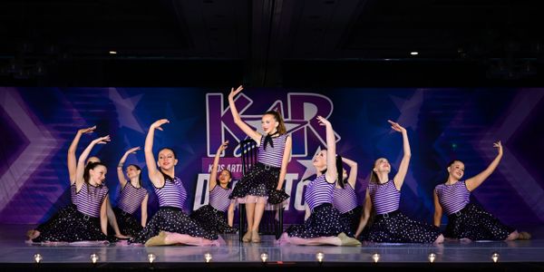 Young dancers in striped tops and polka dot skirts perform on stage.
