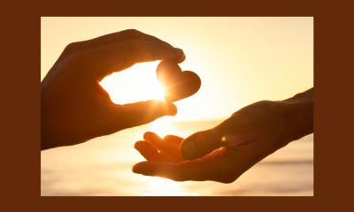 Hand holding heart shape at sunset between open palm.