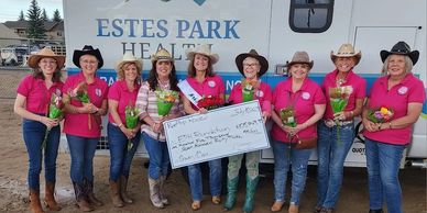 Group of women in cowboy hats holding flowers and a large check at Estes Park Health.