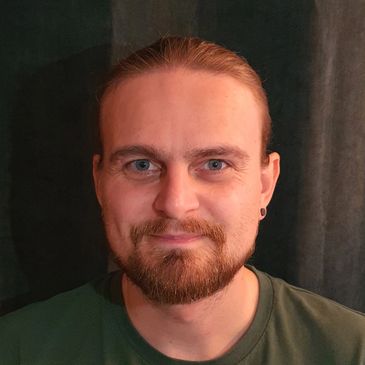 Smiling man with beard and tied-back hair.