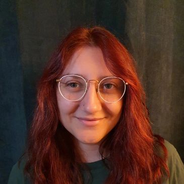 Smiling woman with red hair and glasses.