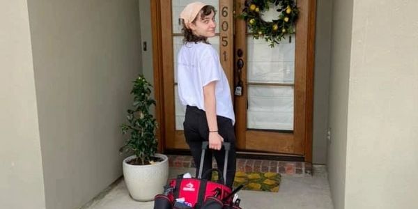Person with a tool bag standing in front of a wooden door.