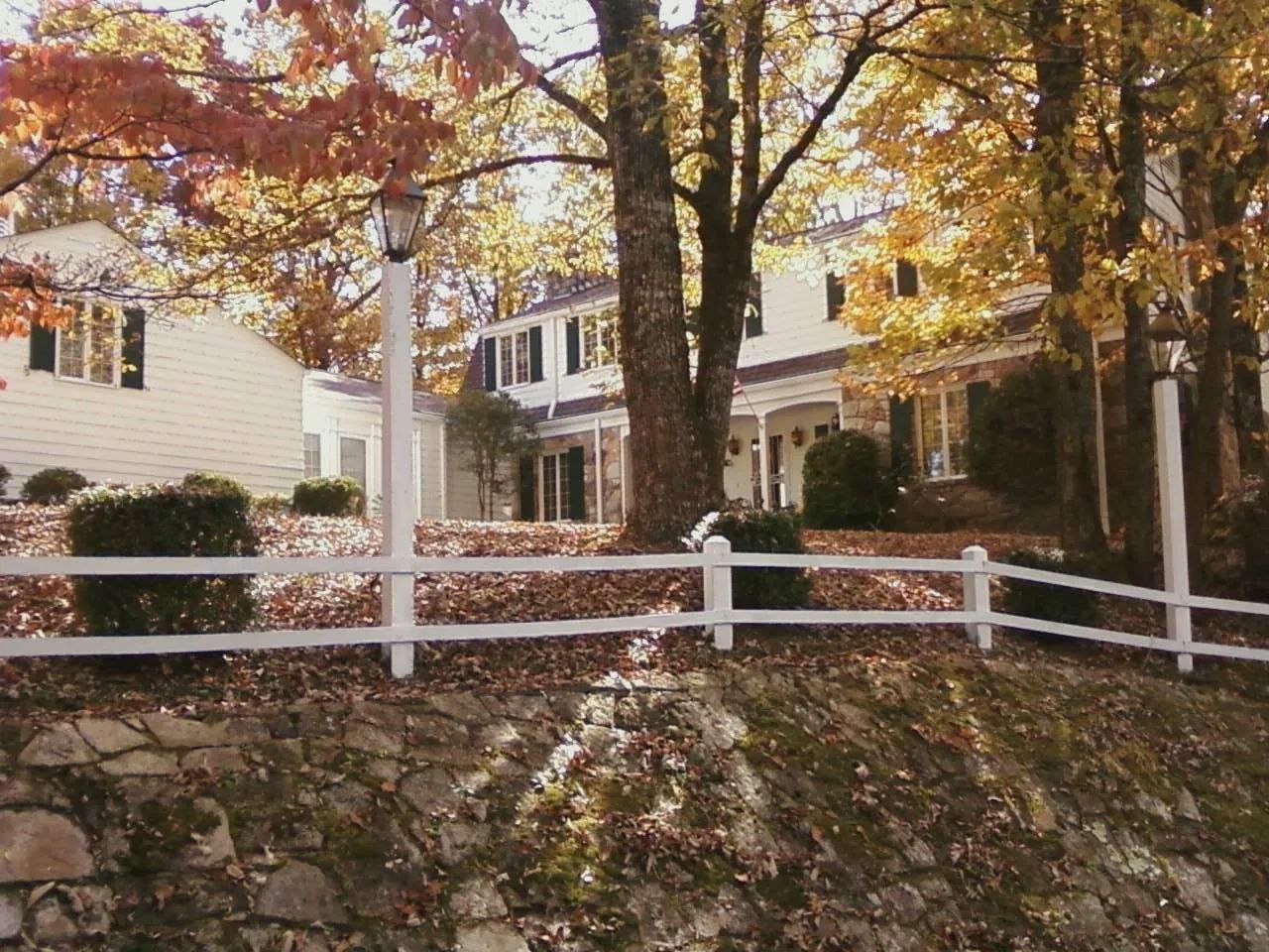 Autumn scene with white house, white fence, and colorful fall foliage.