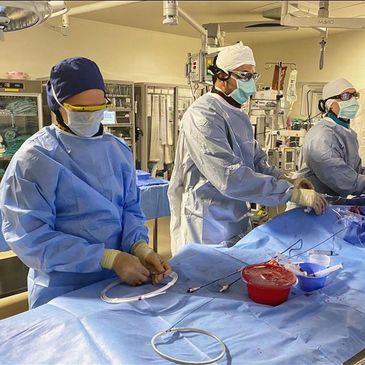 Three surgeons in blue gowns perform a medical procedure in a sterile operating room.