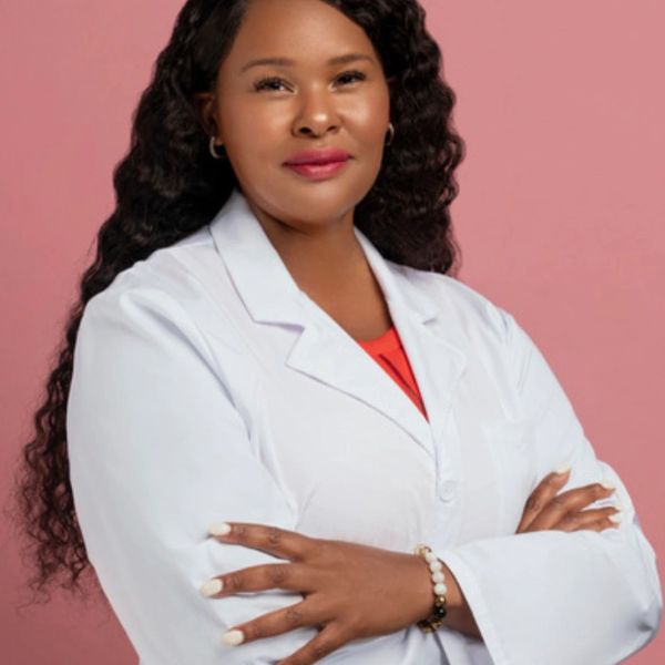 Confident woman in a white lab coat against a pink background.