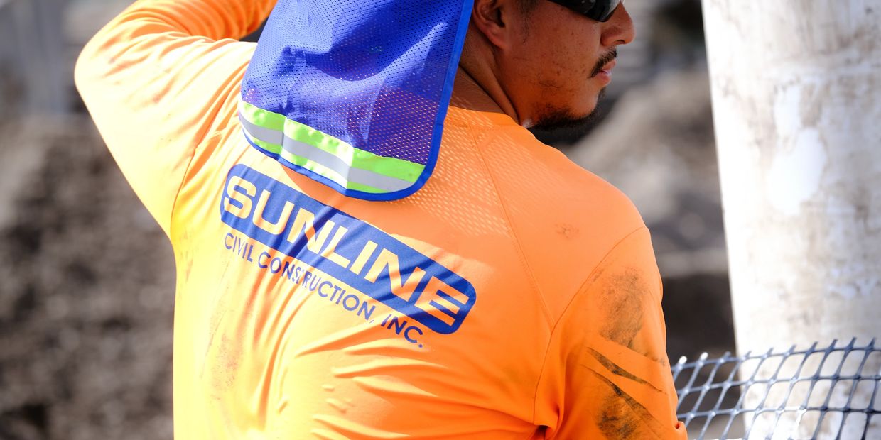 Construction worker wearing a bright orange shirt and blue sun protection.
