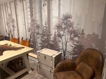 A mural style wallpaper depicting a misty morning forest with deer, trees and shrubs. In grey scale