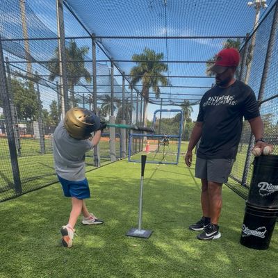 Child hitting a baseball off a tee with coach observing.