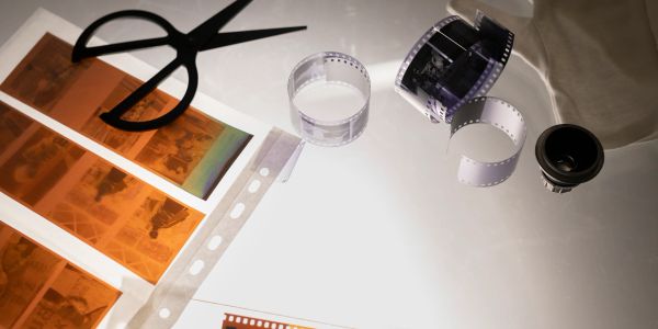 Film negatives, scissors, and camera lens on a light table for photo editing.