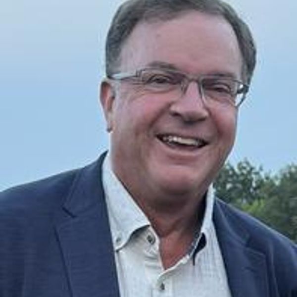 Smiling man wearing glasses and a blazer outdoors.