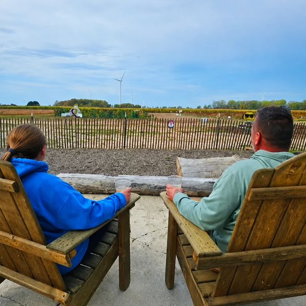 Two people sitting outdoors on wooden chairs, holding drinks.