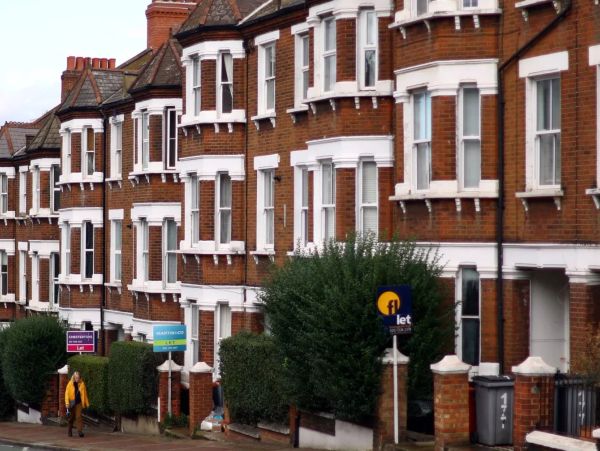 Row of brick houses with "to let" signs and a person walking.