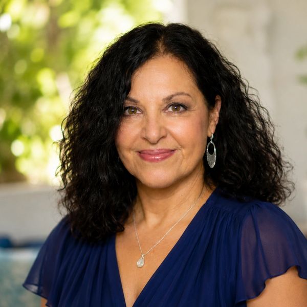 Smiling woman with curly black hair wearing a blue blouse.