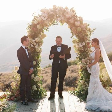 Bride and groom standing under a floral arch during an outdoor wedding ceremony.