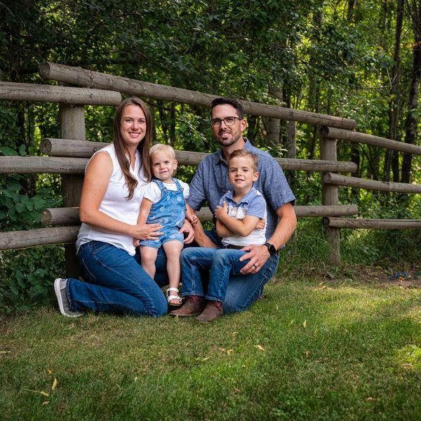 A family of four posing outdoors by a wooden fence.