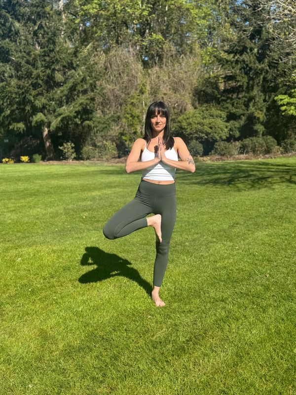 Woman practicing yoga outdoors in a tree pose on green grass.