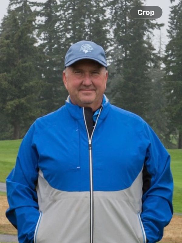 Man in blue and gray jacket and cap on a golf course.