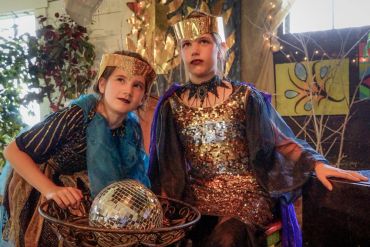 Two kids dressed in shiny king costumes with a disco ball.