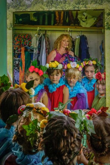 Children in colorful costumes looking in a mirror with a woman behind them.