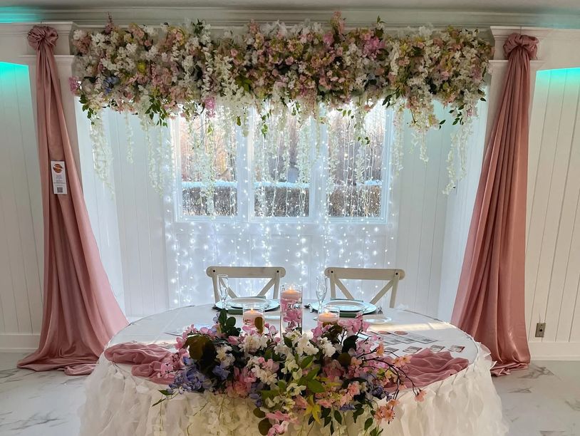 Elegant floral wedding table setup with soft pink drapes and fairy lights.