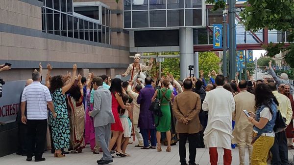 A crowd greets a man dressed as a groom during a festive outdoor event.