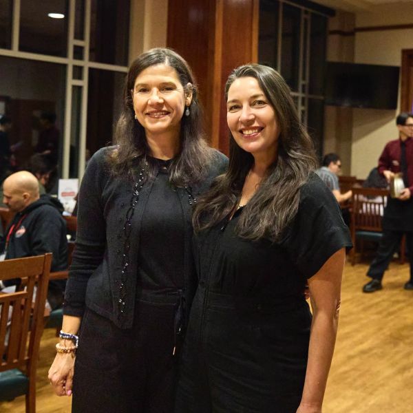 Two women smiling indoors at a social event.