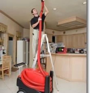 Man vacuuming ceiling with a long red hose.