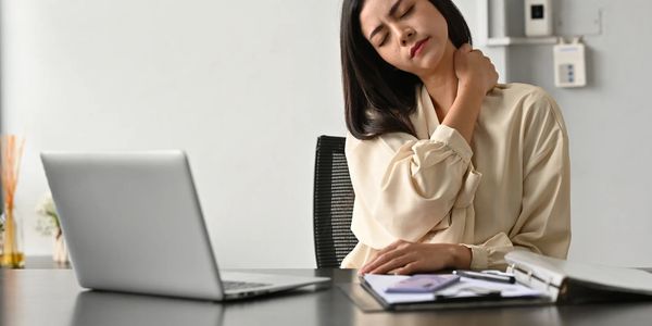 Woman massaging her neck while sitting at a desk with a laptop and documents.