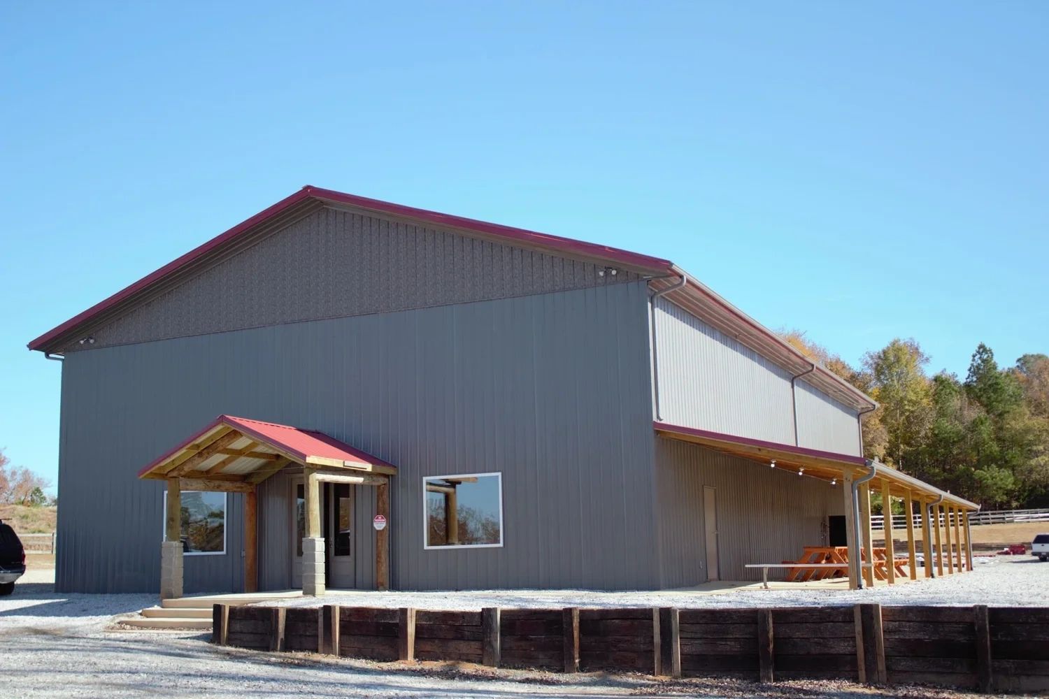 Large gray metal building with red roof and wooden porch.